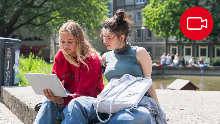 Zwei Studentinnen sitzen mit Laptop auf dem Campus