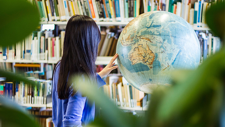 Blick auf eine Frau, die an einem Globus in einer Bibliothek steht.