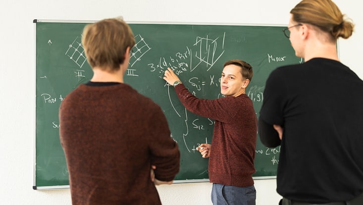Studierende vor einer Kreidetafel.