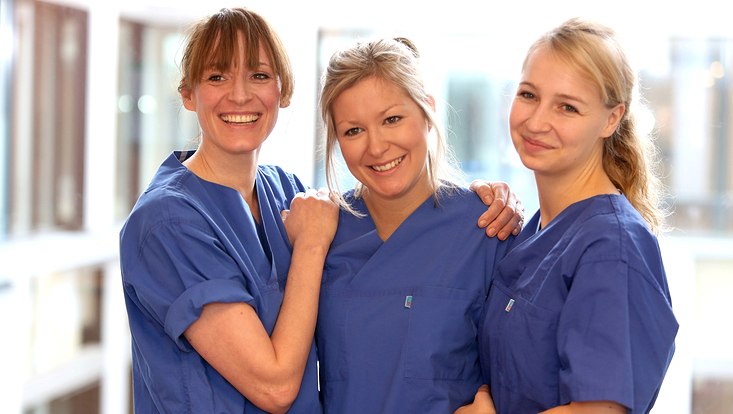 Drei Hebammen stehen zusammen und lächeln.