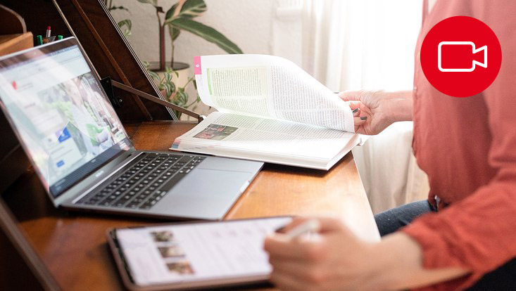Blick auf eine Person, die online mit Laptop, Tablet und Buch studiert.