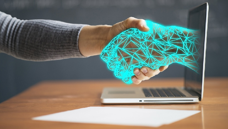 Eine Hand reicht einer künstlichen Hand aus dem Laptop die Hand