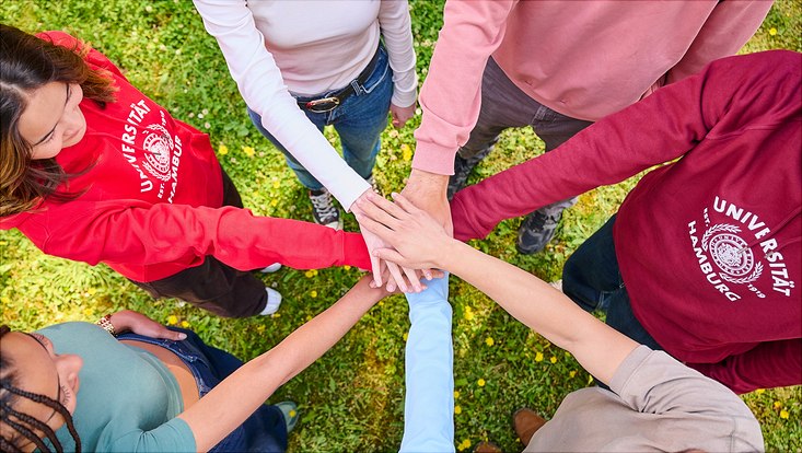 Studierende stehen in einem Kreis und legen ihre Hände aufeinander