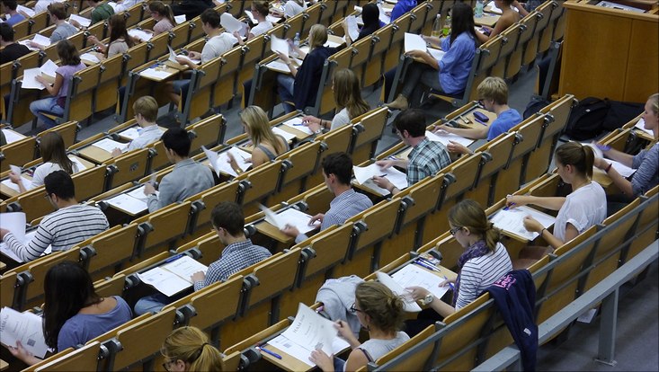 Studierende sitzen in einem Hörsaal und schreiben eine Prüfung