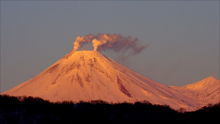 Ein schneebedeckter Vulkan, aus dem Rauch ausbrucht.