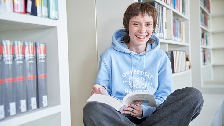 Studierende in der Bibliothek mit einem Buch in der Hand.