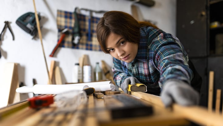 Blick auf eine Frau, die Holzbretter bearbeitet.